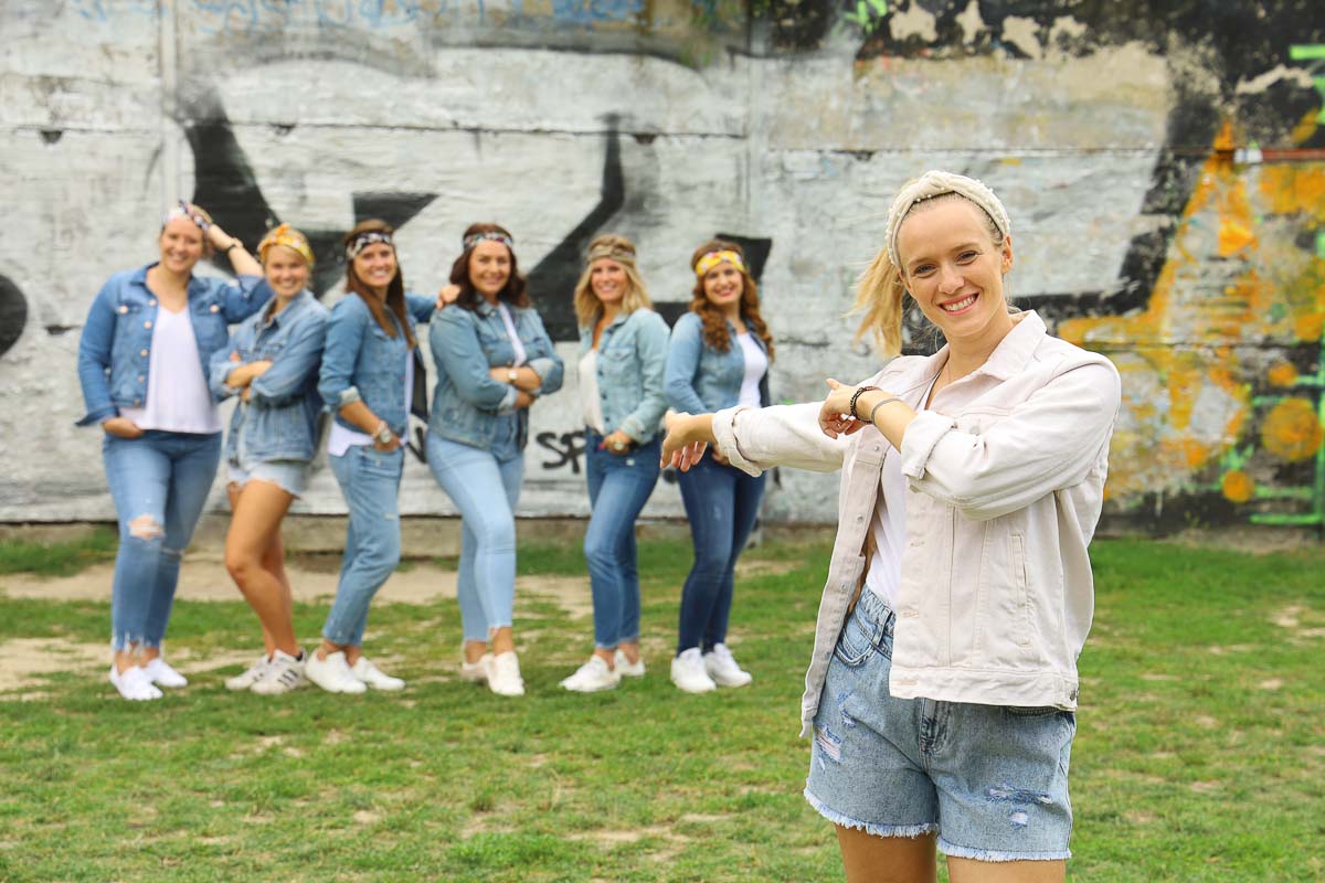 Bei einem JGA Fotoshooting von Junggesellinnen zeigt die Braut im Vordergrund auf ihre lächelnden Freundinnen im Jeans-Outfit