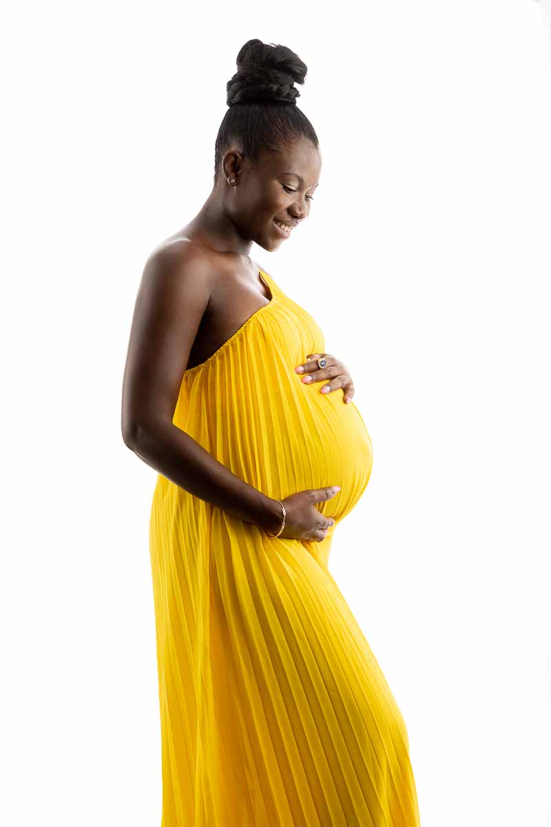 Fotoshooting einer schwangeren dunkelhäutigen Frau, die stolz unter einem weißen Kleid ihren Babybauch zeigt