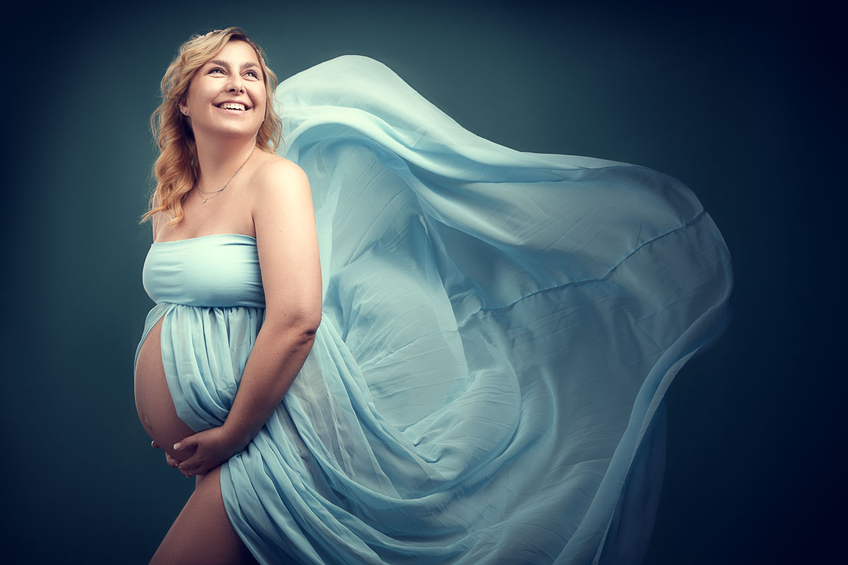 Fotoshooting einer schwangeren, glücklich lachenden, blonden Frau in einem türkis-blauem Kleid
