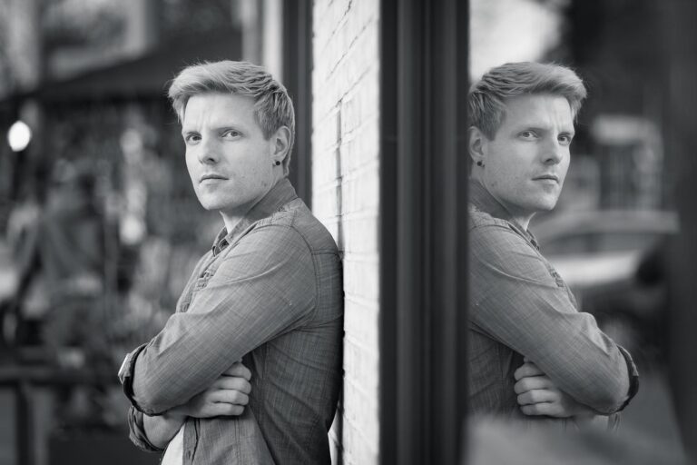 Dating-Foto eines ernst blickenden jungen blonden Mannes in einem Jeanshemd, dessen Gesicht in einer Scheibe spiegelt