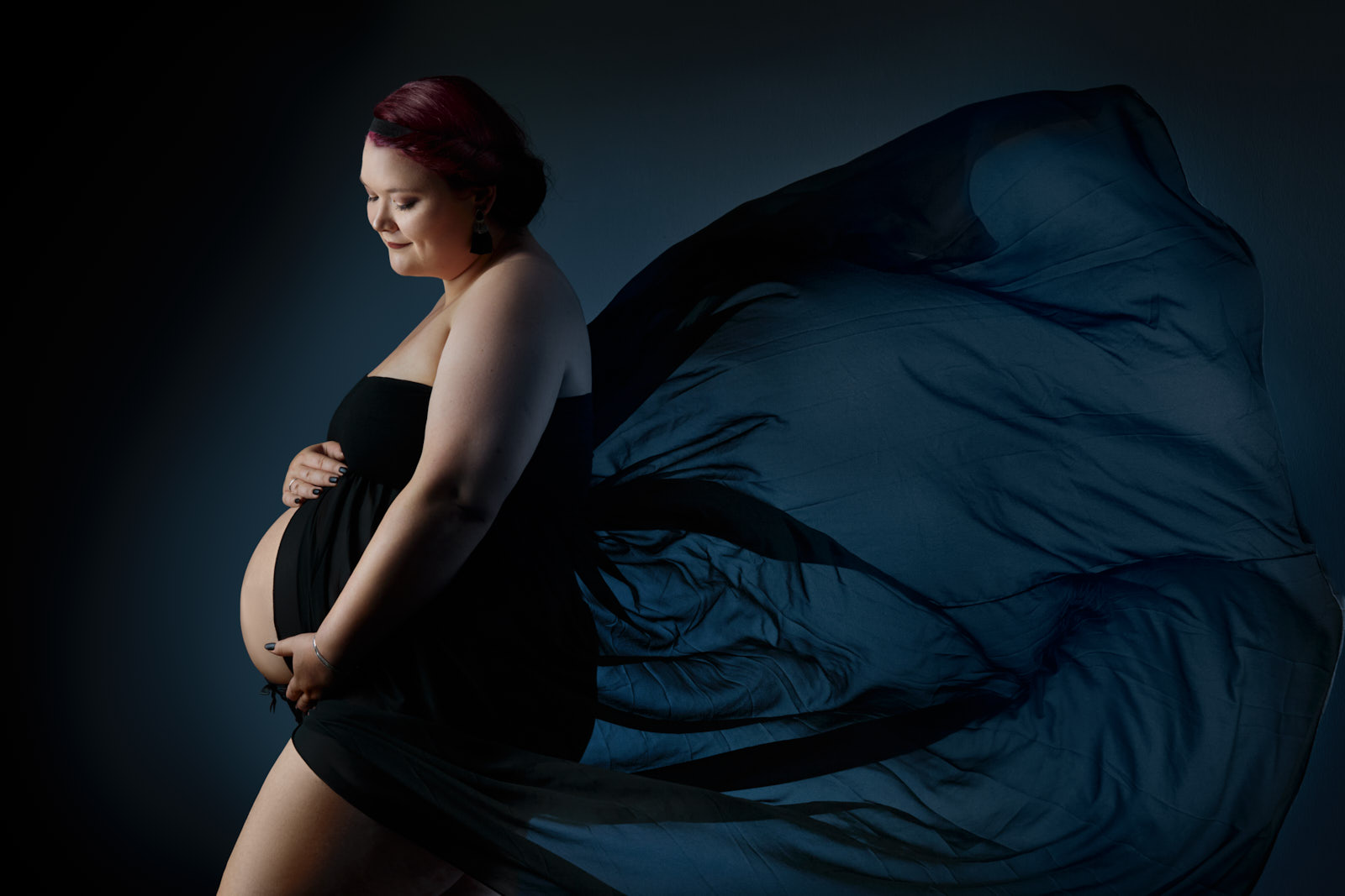 Fotoshooting einer schwangeren, glücklich lachenden,rothaarigen Plus-Size Frau in einem schwarzen Kleid, das elegant weht.