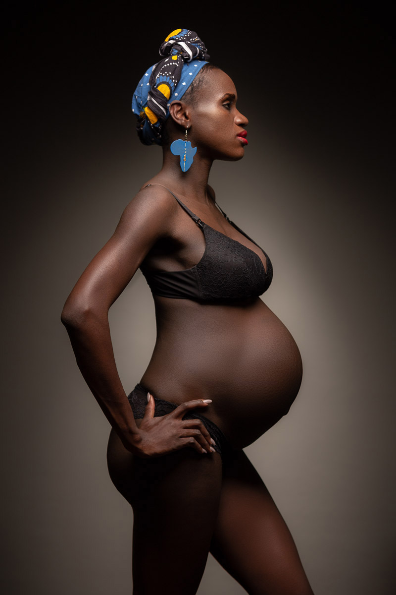 Fotoshooting einer schwangeren dunkelhäutigen Frau, die im Profil steht und ihren Babybauch zeigt