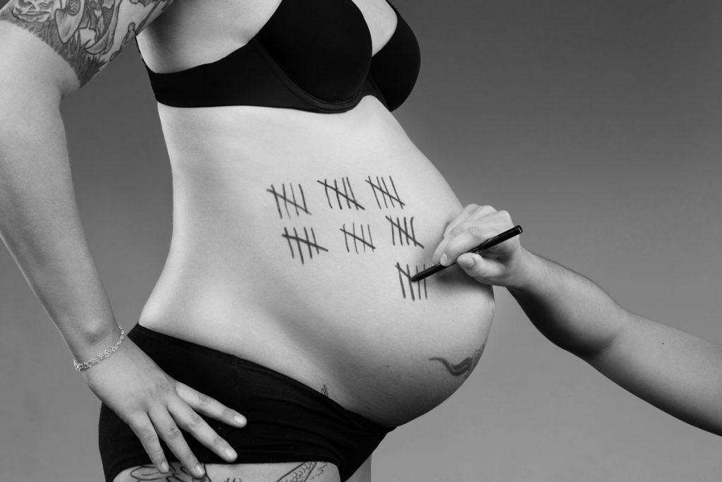 Eine Hand macht mit einem Stift eine Strichliste auf dem Babybauch einer schwangeren Frau