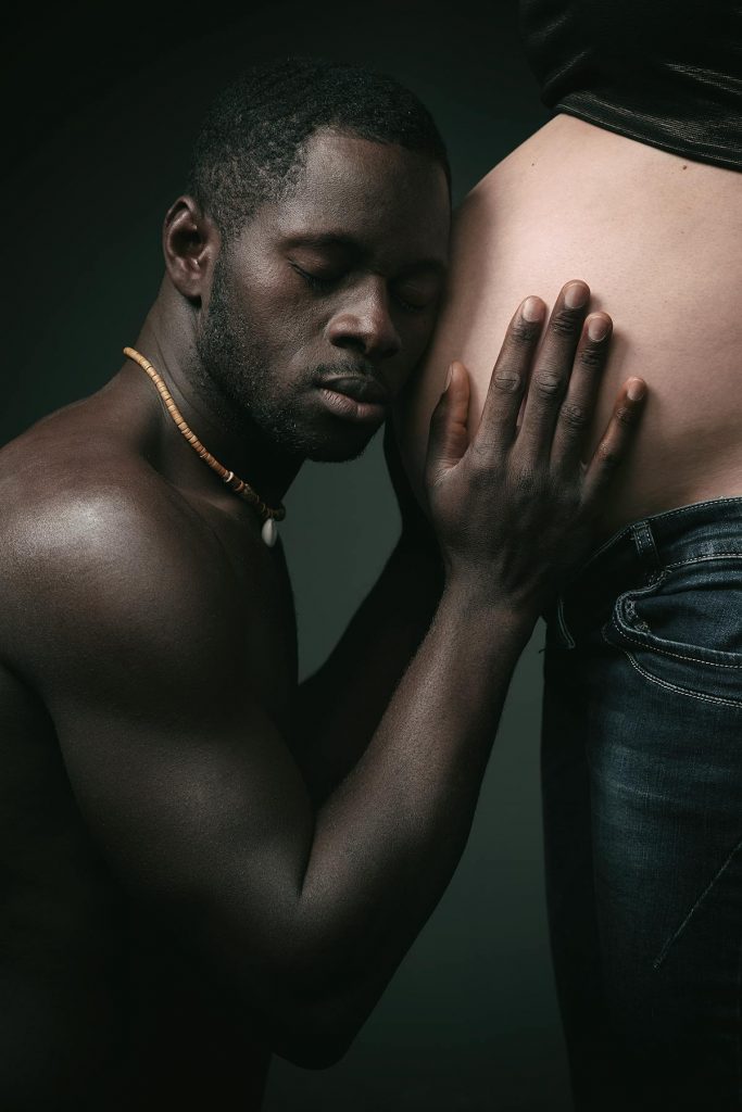 Dunkelhäutiger, werdender Vater hört liebevoll am Babybauch seiner schwangeren Frau.