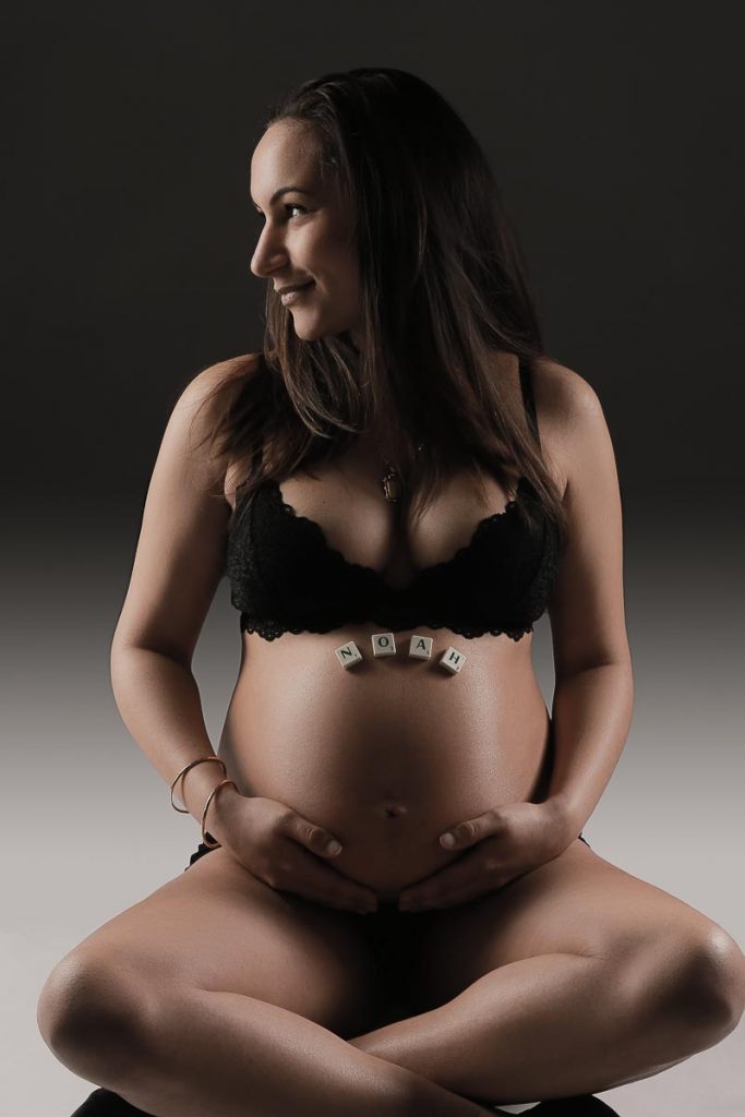 Foto einer schwangeren Frau auf deren Bauch mit Scrabbelsteinen der Name des Kindes geschrieben steht.