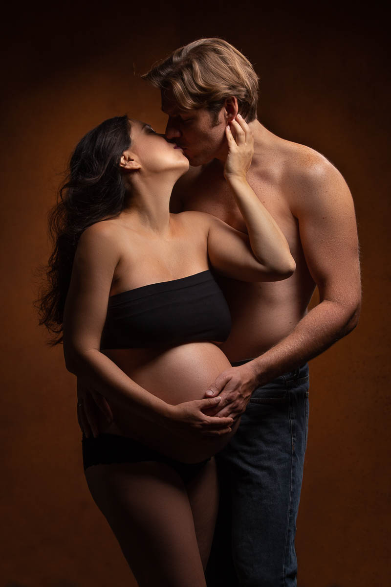 Schwangere Frau mit dickem Babybauch küßt Ihren Mann und berührt zart die W...