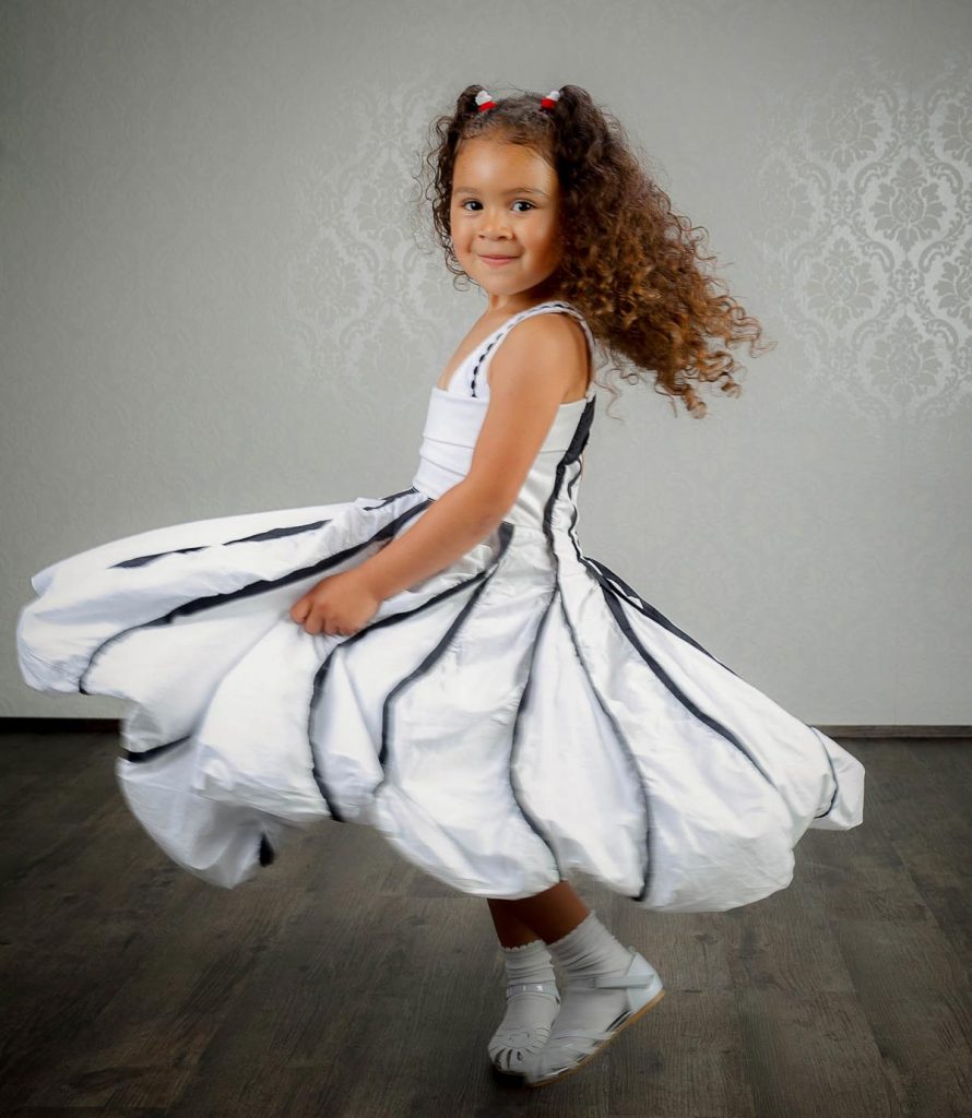 Kleines, dunkelhäutiges Mädchen tanzt in weißem Kleid