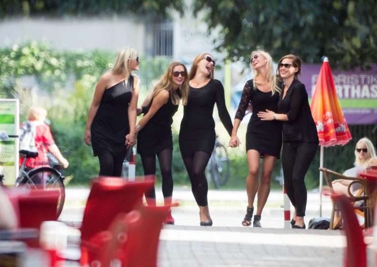 Fünf junge Frauen in schwarzen Cocktailkleidern haben Spaß bei Ihrem JGA Junggesellinnenabschied Fotoshooting.