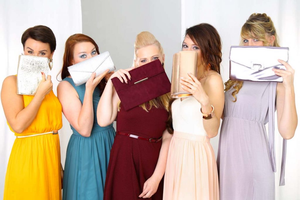 Fünf junge Frauen verstecken sich beim JGA-Fotoshooting bei Ihrem Junggesellinenabschied im Fotostudio Farbtonwerk in Berlin hinter Ihren zu Ihren farbigen Kleidern passenden Handtaschen.