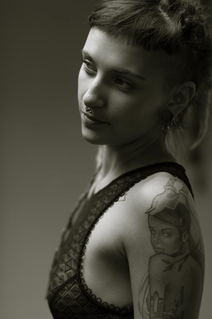 Schwarzweiß Portraitfoto einer Frau mit Tattoos und Nasenpiercing