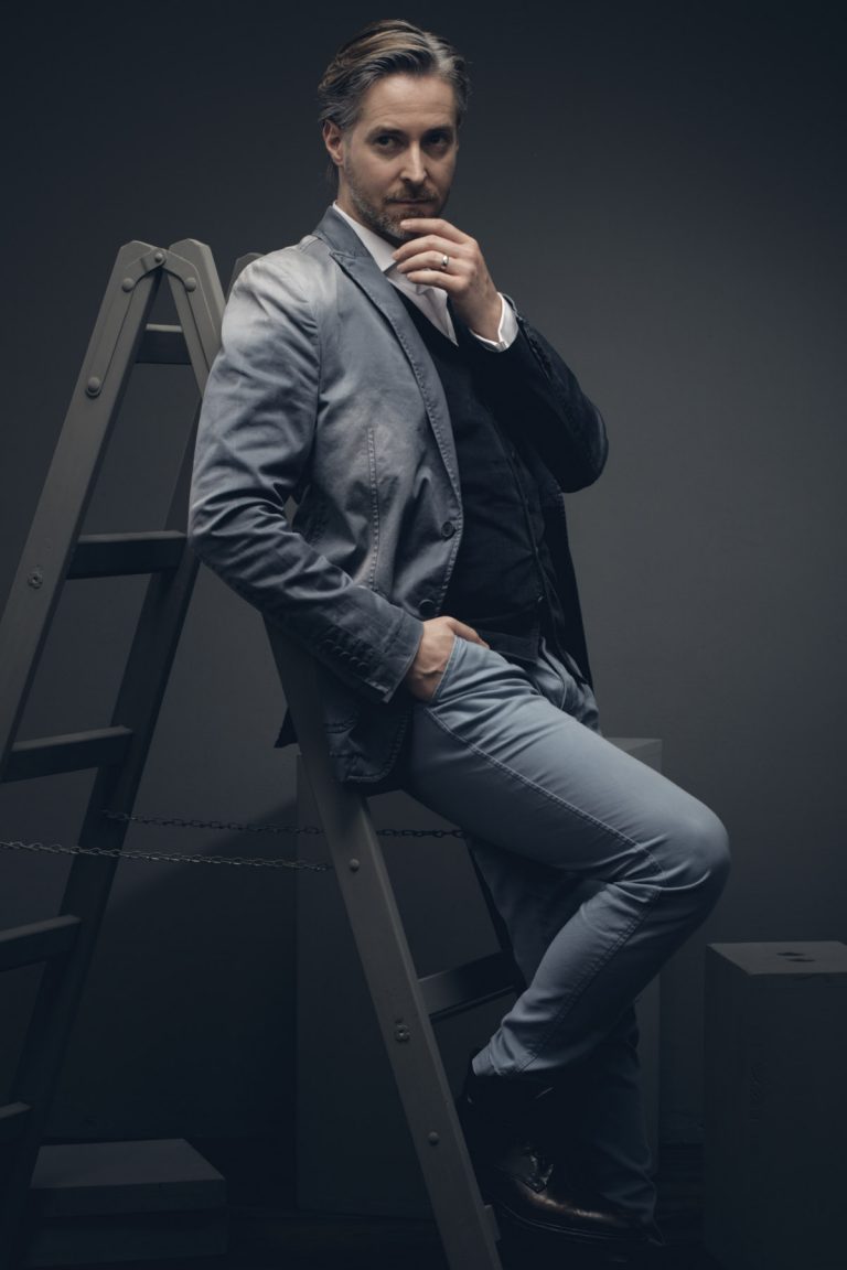 Künstlerportrait eines Schauspielers, der ein nachdenklich an einer graue Leiter lehnt